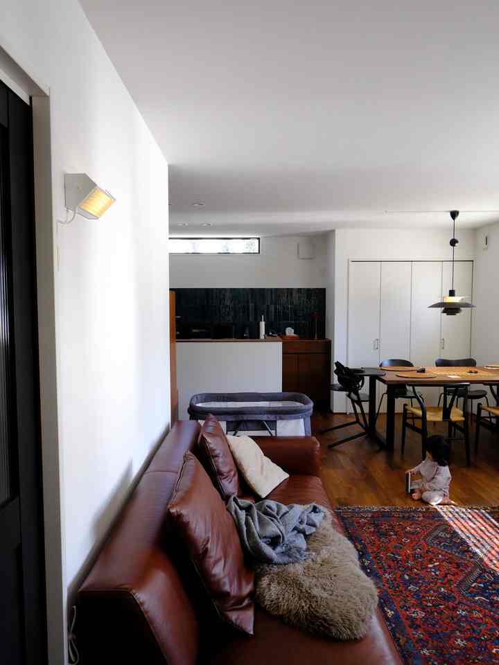 温かみのある木目調と茶色のレザーソファが置かれたリビングとダイニングルーム、ラグの上で遊ぶ赤ちゃんがいる落ち着いた空間