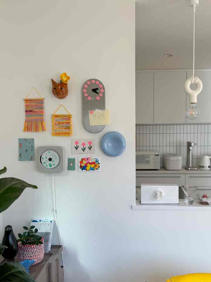 白い壁とキッチンが一体化した空間、壁にはカラフルな装飾と青い皿が配置され、シンプルで自然な雰囲気のインテリア