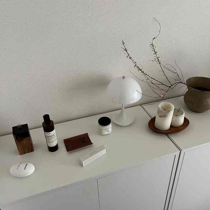 白とナチュラルトーンのワンルーム、シンプルなキャビネット上にキャンドルやテーブルランプなどのオブジェが配置された印象的な空間