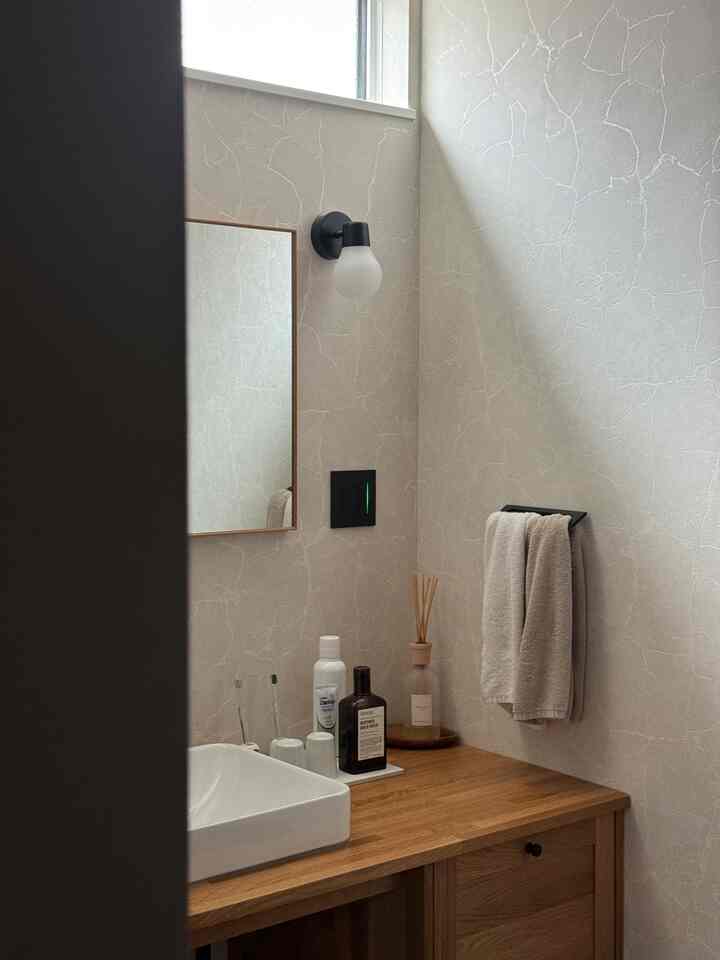 ナチュラルな木目調と白を基調としたバスルーム、鏡とタオル、ディフューザーが配置された雰囲気のあるインテリア