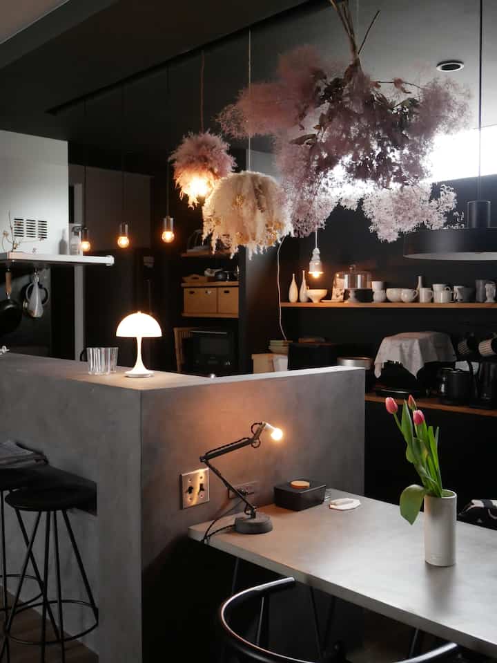 Modern kitchen with dark gray and black tones, accented by white Panthella table lamp and dried flowers in a natural setting