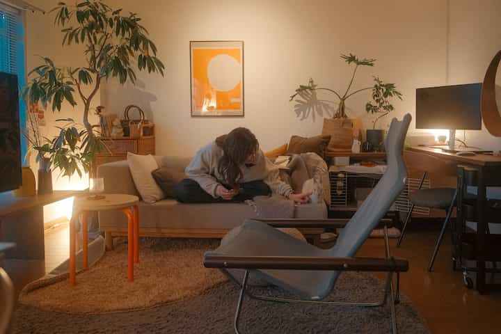 温かみのあるブラウン調の1LDKリビング、ベージュソファと観葉植物、自然な雰囲気のワークスペースが配置された空間