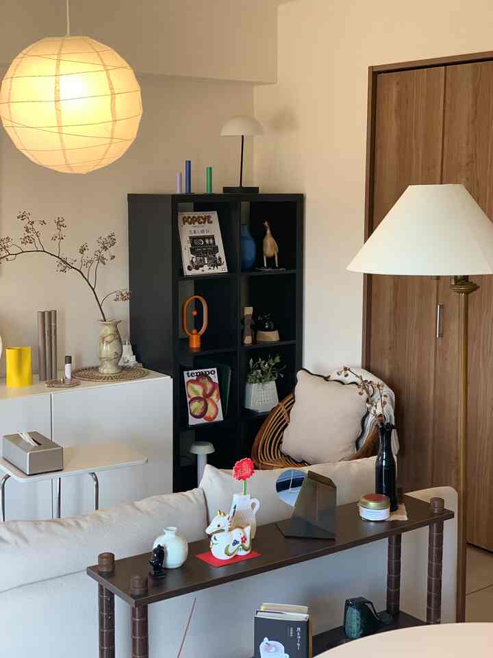 A modern and neat living room in white and brown tones featuring a sofa, shelves, and a dining table