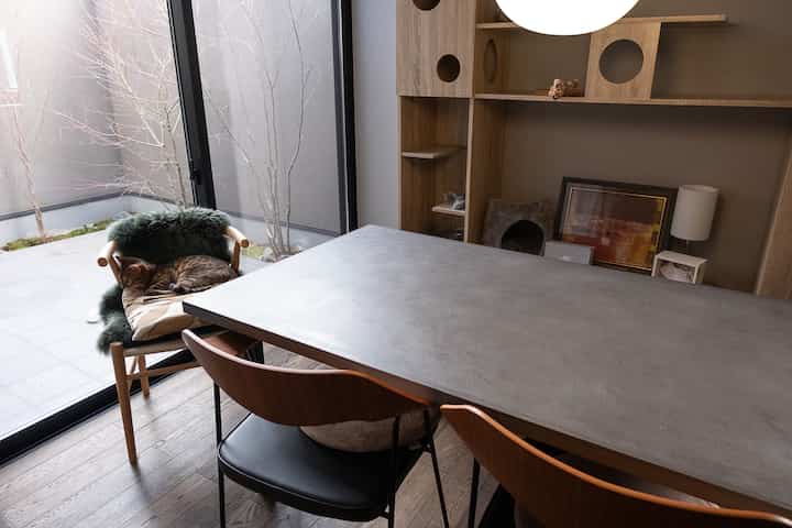 木目調とコンクリートが調和したモダンなダイニング、窓辺で猫が寛ぐ雰囲気のあるインテリア