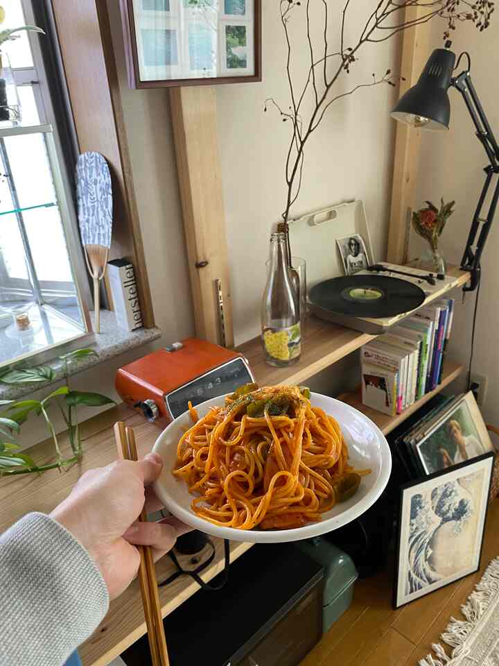 木目調とオレンジ色が調和する一人暮らしの空間、デスク上にナポリタンパスタの皿が置かれている印象的なインテリア