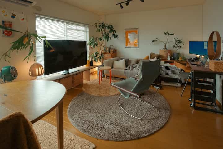 ナチュラルな色調の12畳リビング、ソファやテレビ、植物、ホームオフィスが調和した印象的な空間