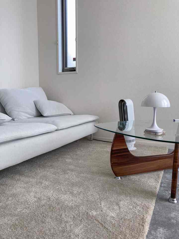 マットホワイトとナチュラルブラウンのトーンの一人暮らしリビング、シンプルなソファとガラスのコーヒーテーブルが配置された清潔感のあるインテリア