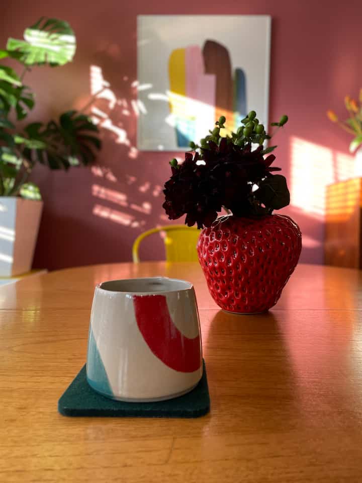 ピンクの壁と木製のダイニングテーブル、イチゴ型の花瓶が配置された温かみのあるカフェ風ダイニング空間