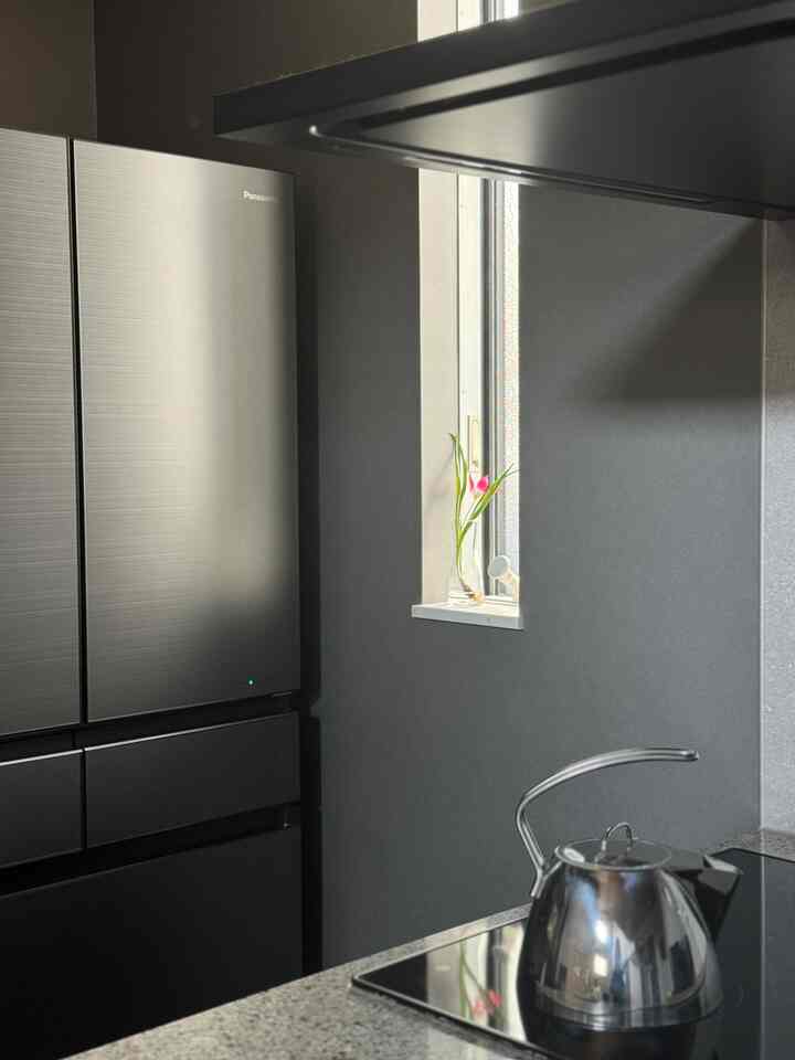 黒い壁とステンレス製冷蔵庫があるモダンなキッチン、コンロの上にステンレスのケトルが置かれている印象的な空間