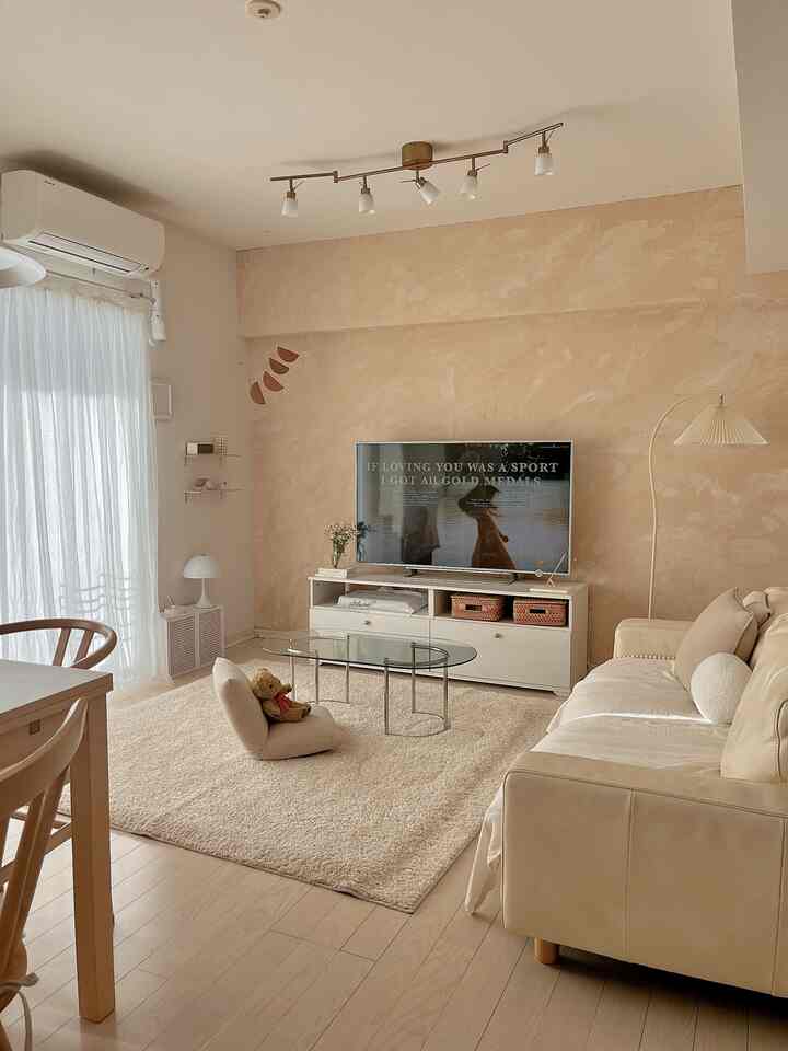 Ivory and natural toned living room featuring sofa, rug, and transparent coffee table with warm and cozy atmosphere