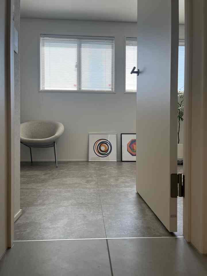 白とグレーのトーンの子供部屋、2つの抽象アートポスターとグレーのアームチェアが配置されたシンプルでミニマルな空間