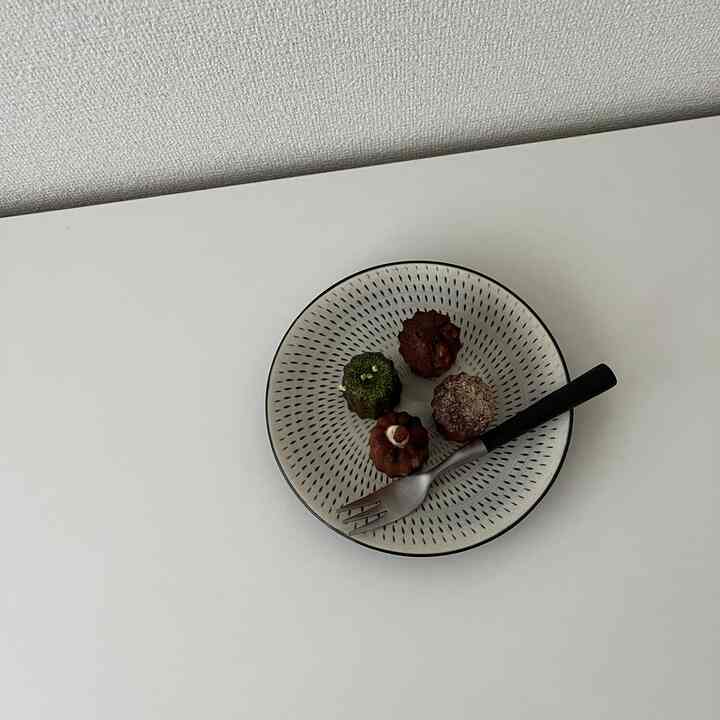 White-toned simple table featuring a patterned plate with four caneles and a small black-handled fork, creating a clean atmosphere