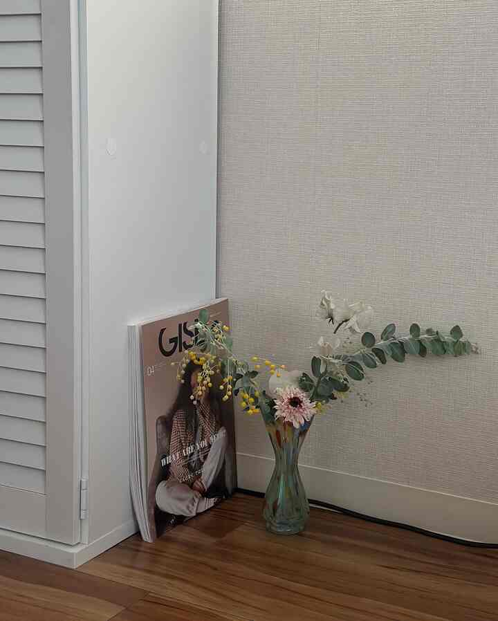 Natural style space with white walls, wood tone floor, corner featuring a vase with flowers and stacked magazines