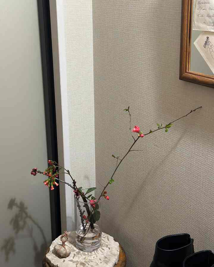 ベージュ調の壁と木製の台に透明な花瓶と自然な枝が置かれたシンプルな玄関スペース