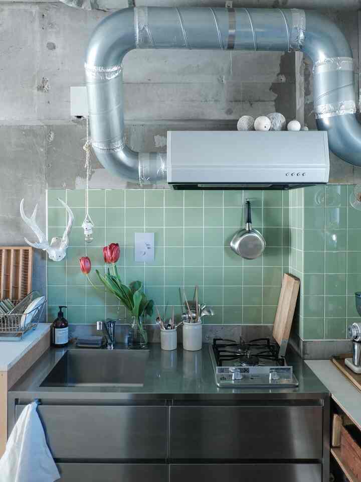 Industrial style kitchen with green tile backsplash, stainless steel cookware, and red tulips in a vase, featuring a minimal aesthetic