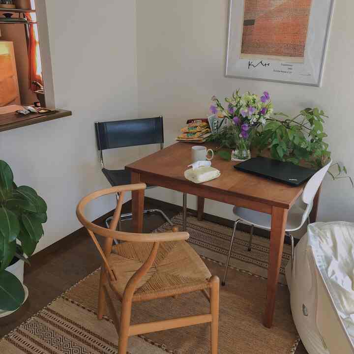 ナチュラルなブラウンのダイニングテーブルと椅子が配置された温かみのあるダイニングルーム、花瓶とノートパソコンが雰囲気を演出