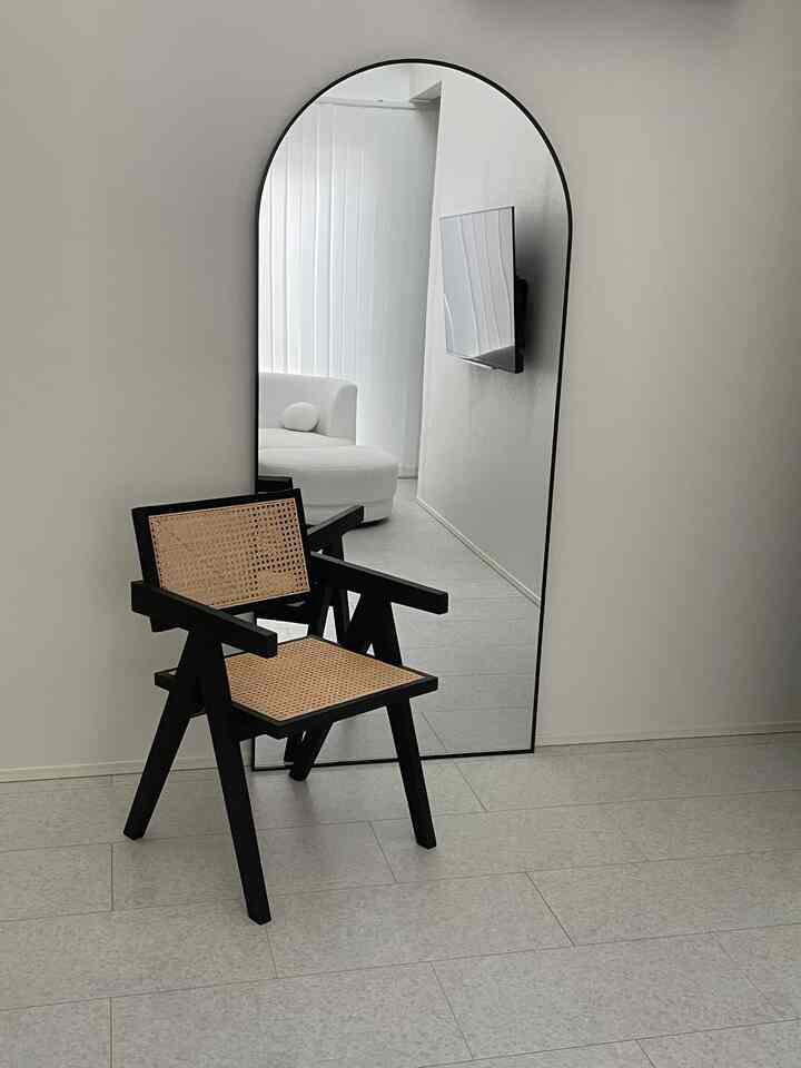 Modern living room in white and black tones featuring a large arched mirror and a rattan chair with a minimalist vibe