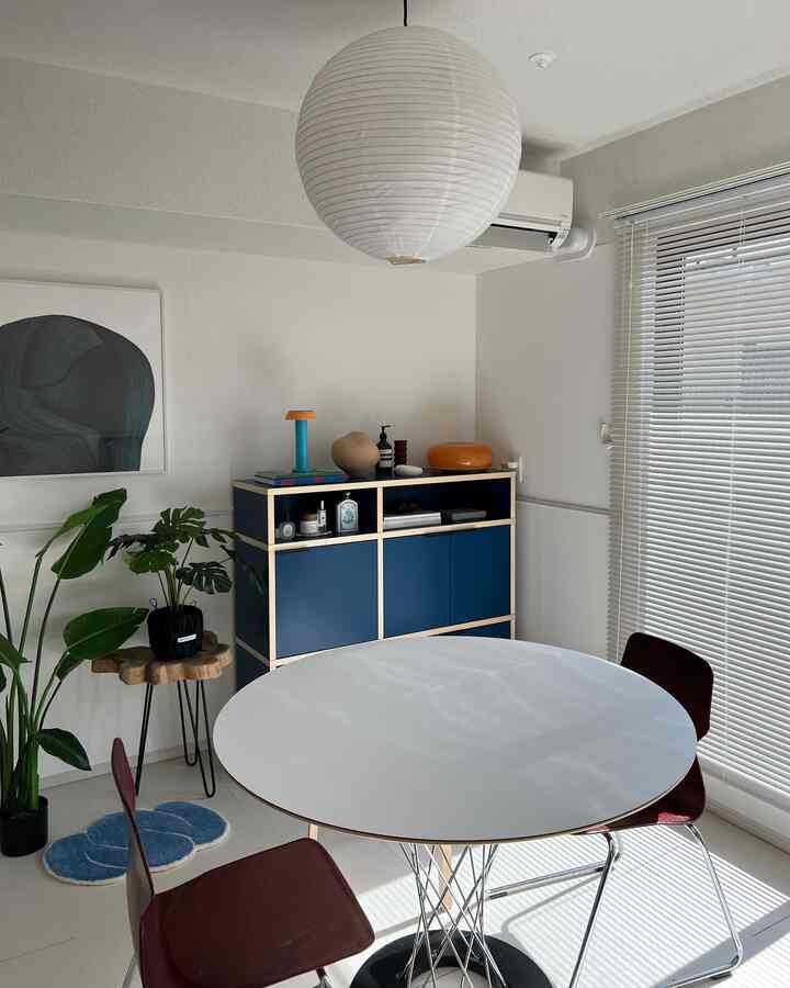 ホワイトとネイビートーンのダイニング、丸テーブルとネイビーの棚、植物が配置されたシンプルモダンな雰囲気のインテリア