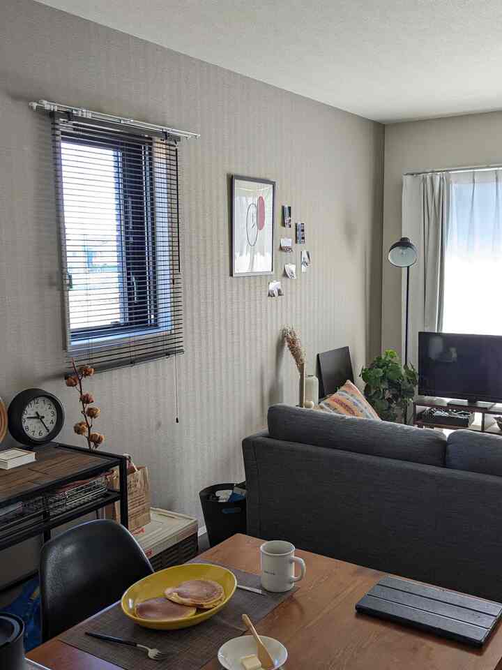 Beige-toned living room for two with wooden dining table, gray sofa, and blinds creating a modern harmonious space