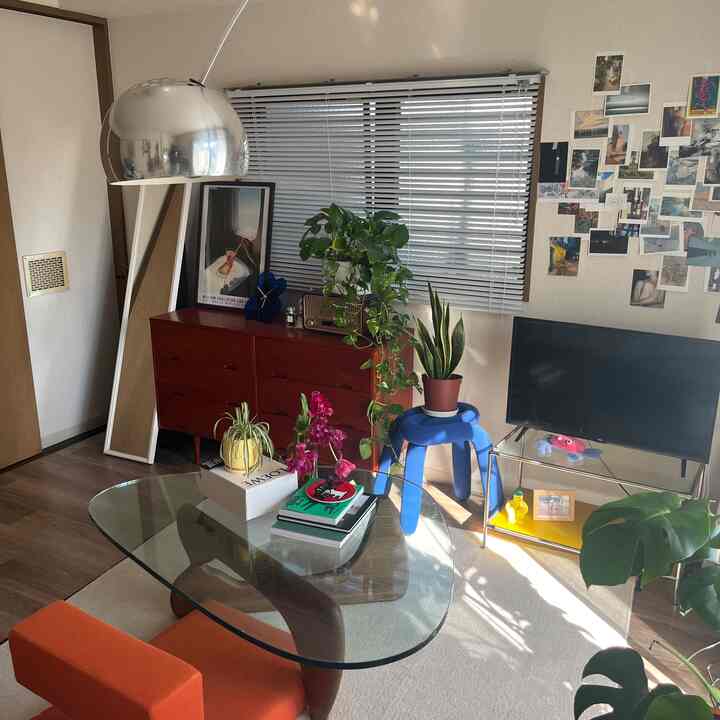 Warm red and orange toned living room featuring a glass table, floor lamp, plants, and a tall mirror, creating a cozy atmosphere
