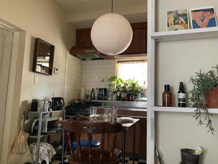 A cozy kitchen with white walls and wood-toned furniture, featuring a paper lantern and plants creating a natural atmosphere