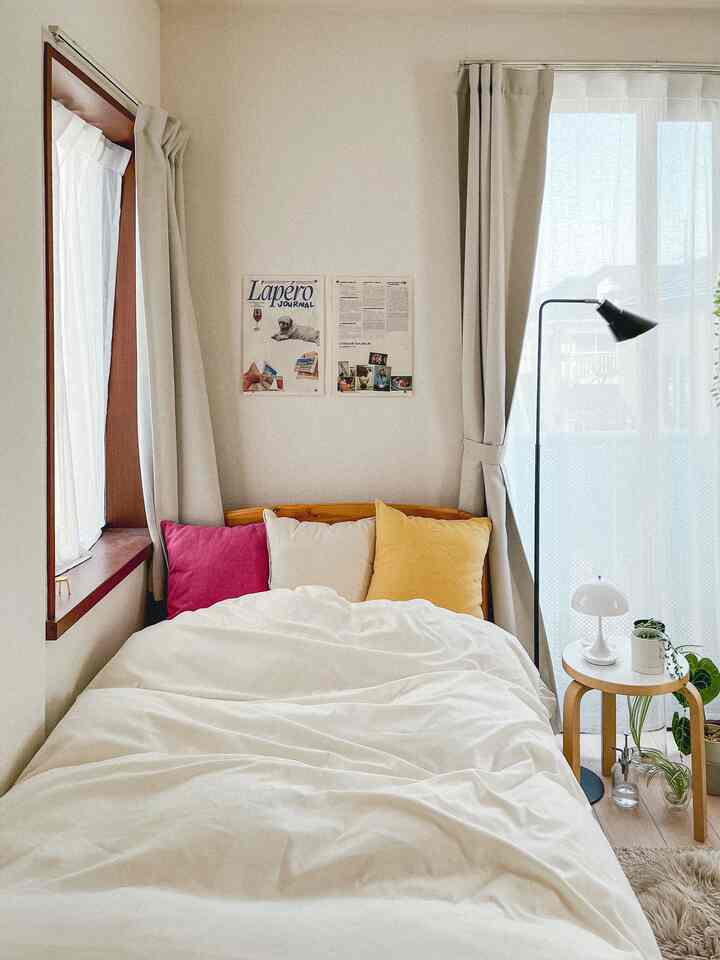 白とナチュラルカラーの寝室、ベッドと枕、ナイトテーブル、フロアランプが配置されたシンプルで温かみのあるインテリア