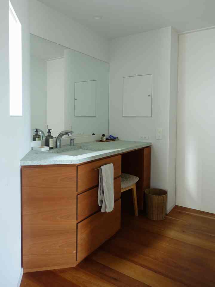 白い壁と木製の洗面台が配置されたナチュラルな雰囲気のきれいなバスルームの洗面スペース