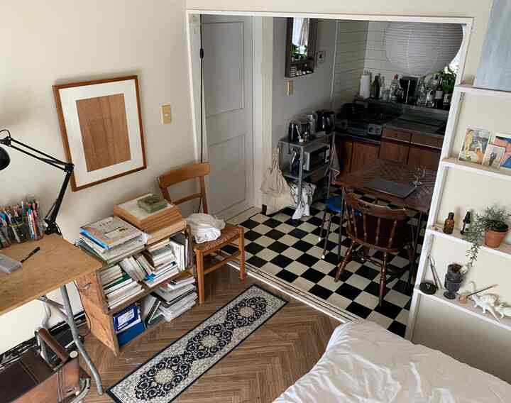 White and wood tone studio apartment featuring a bed and desk, creating a cozy atmosphere in a compact living space