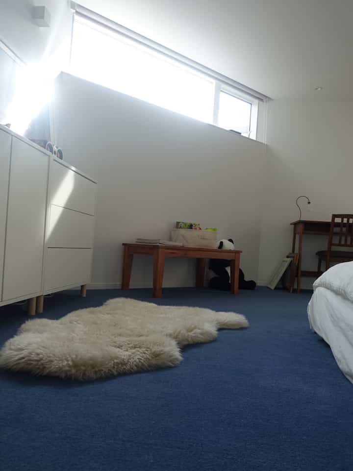 青いカーペットの寝室、木製家具とクリーム色のファーラグが配置された雰囲気のあるインテリア