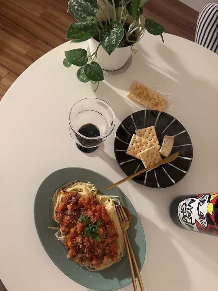 白いテーブルに植物とスパゲッティ、クラッカーが置かれたシンプルで自然な雰囲気のホームカフェ