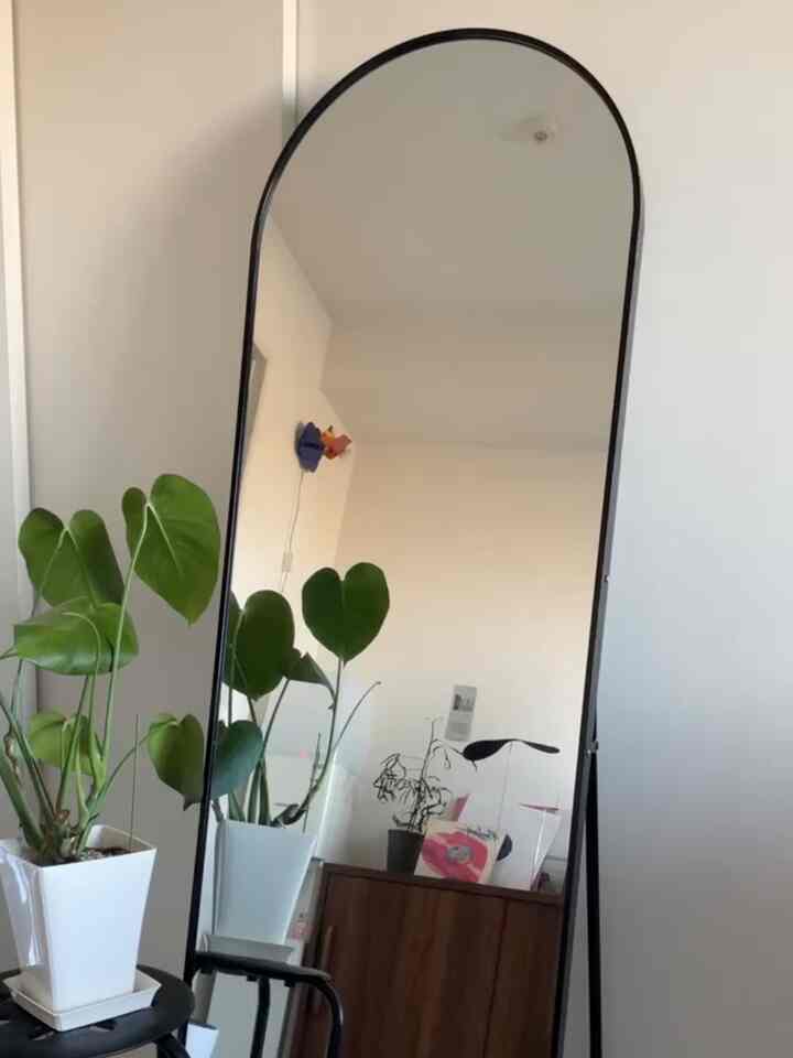 白い壁と木製キャビネットのモダンなリビング、大きなモノトーンの鏡とモンステラの植物が空間を広く見せる印象的なインテリア