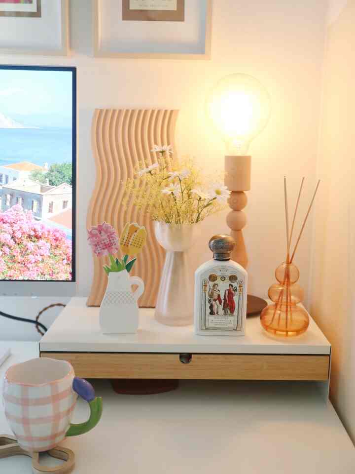 White and natural color home office space with a desk featuring a vase of flowers and a table lamp arranged for a cozy workspace