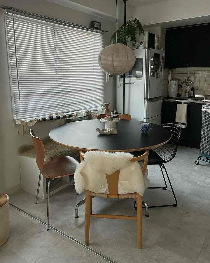 A calm dining room with black and brown wood tones, featuring white blinds and a pendant light in a simple single household space