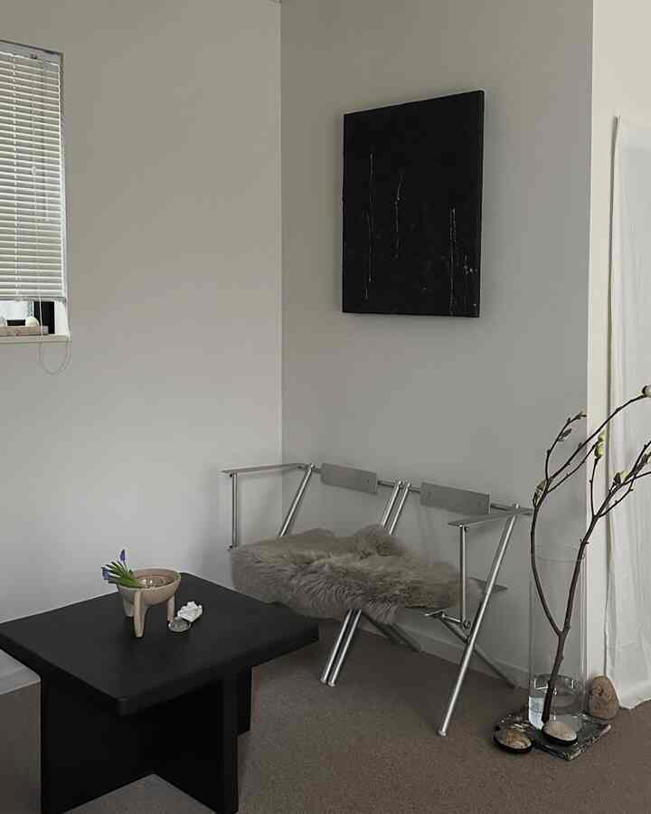 白い壁と黒いコーヒーテーブルのあるコンパクトなリビング、金属フレームのベンチと自然な印象の花瓶が配置された落ち着いた空間