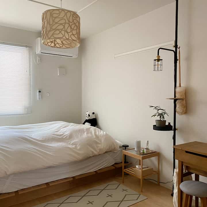 ナチュラルカラーのモダンな寝室、木製ベッドフレームとナイトテーブル、フロアランプが配置された落ち着いた空間