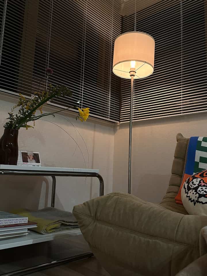 ナチュラルカラーのリビング、ベージュのソファとサイドテーブルの花瓶、ムード照明のフロアランプが配置された雰囲気のあるインテリア