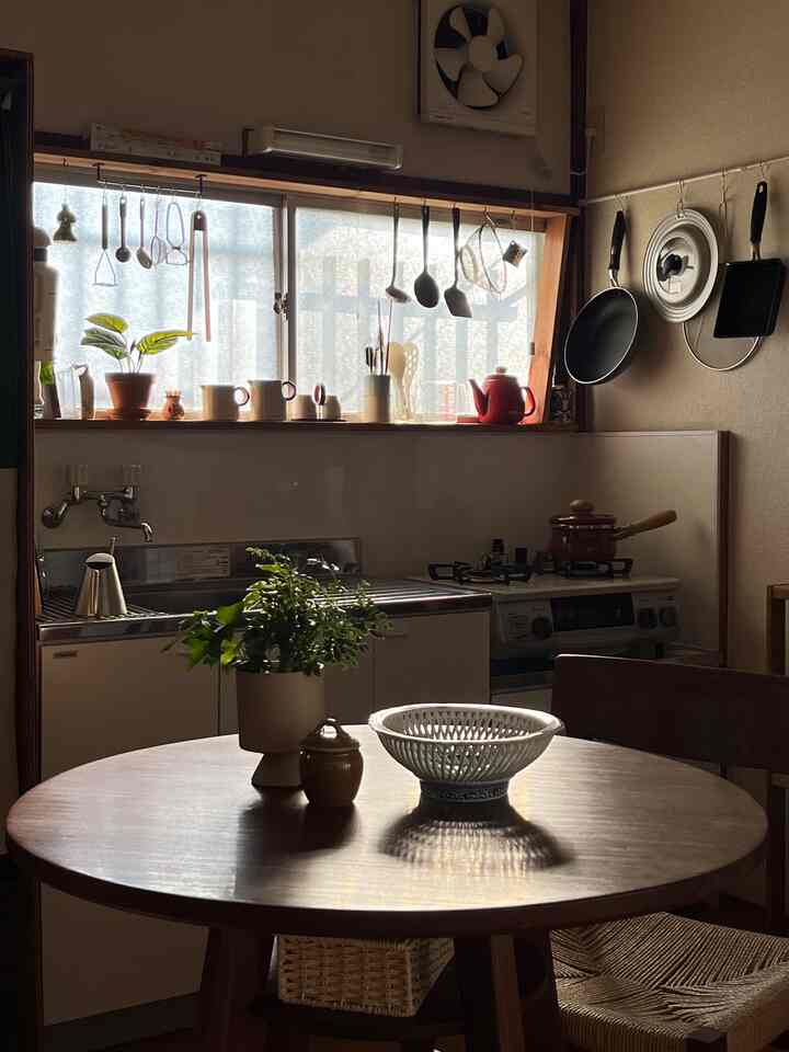 ベージュとブラウン調のキッチン、丸いダイニングテーブルに植物と器が置かれた温かみのある一人暮らしの空間