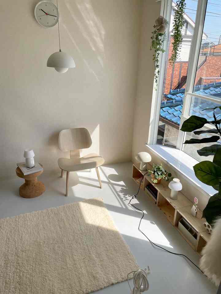 Bright white and wood-tone living room with natural light pouring through the window, featuring a lounge chair and lamps in a clean space