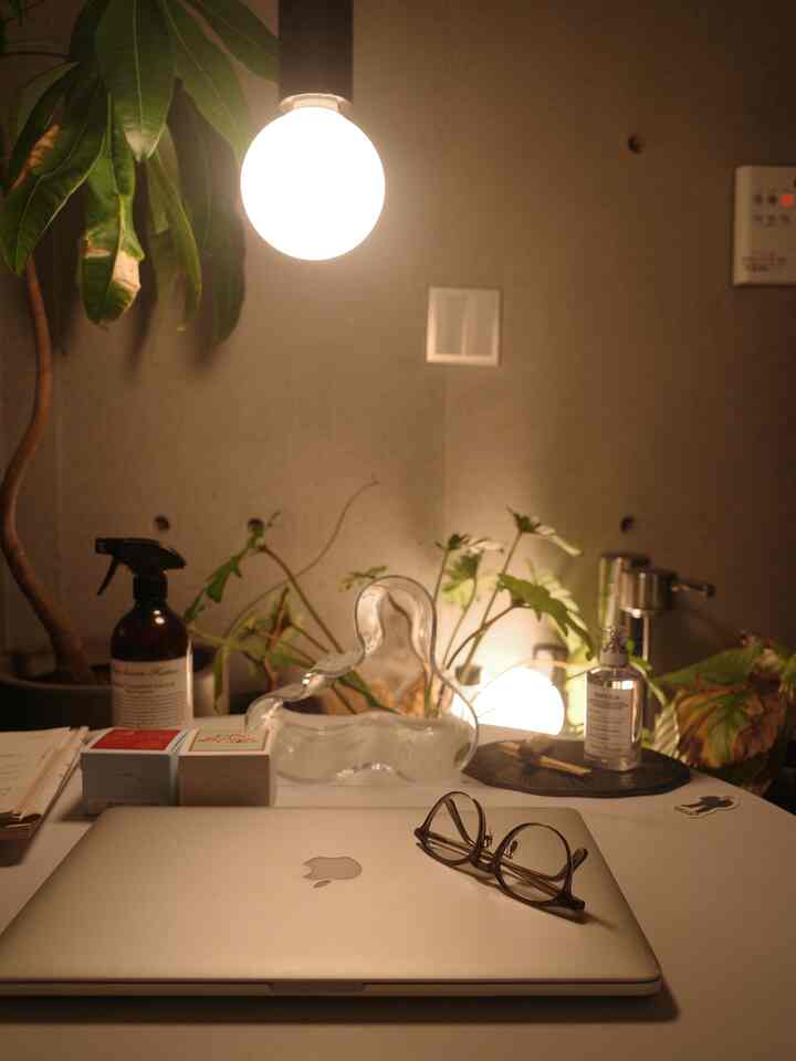 暖かい照明と植物があるモダンなホームオフィス空間、テーブルの上にノートパソコンと眼鏡が置かれている