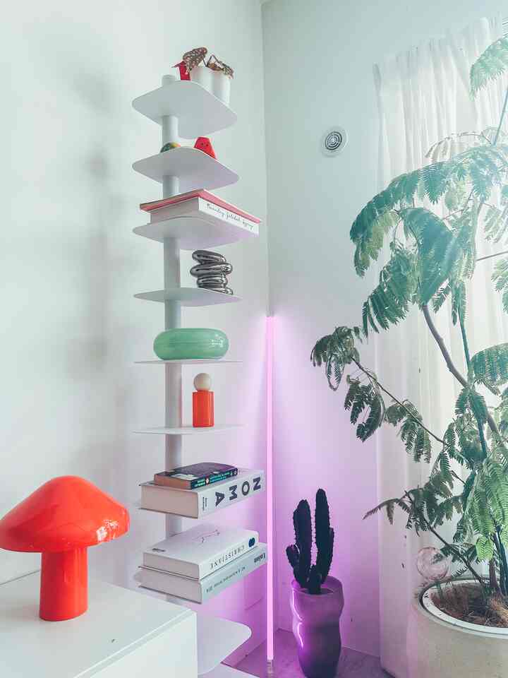 White and natural tone studio apartment study space featuring a shelf, table lamp, and plants with a calm atmosphere