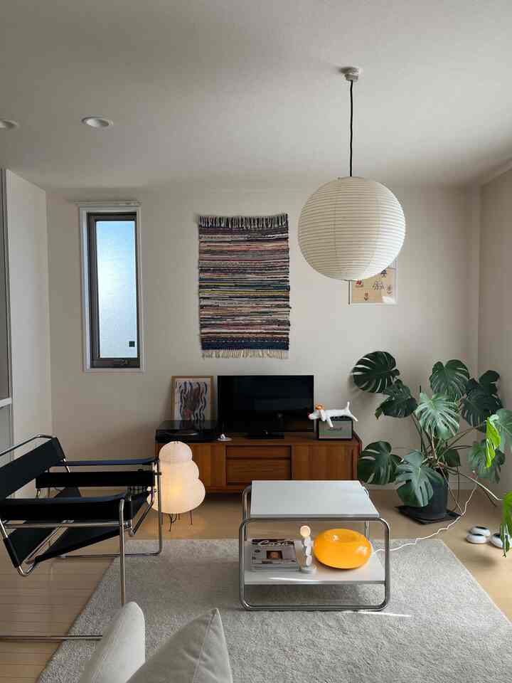 白い壁と木目調のテレビ台のあるモダンなリビング、黒い椅子と大きな観葉植物が配置されたシンプルな空間