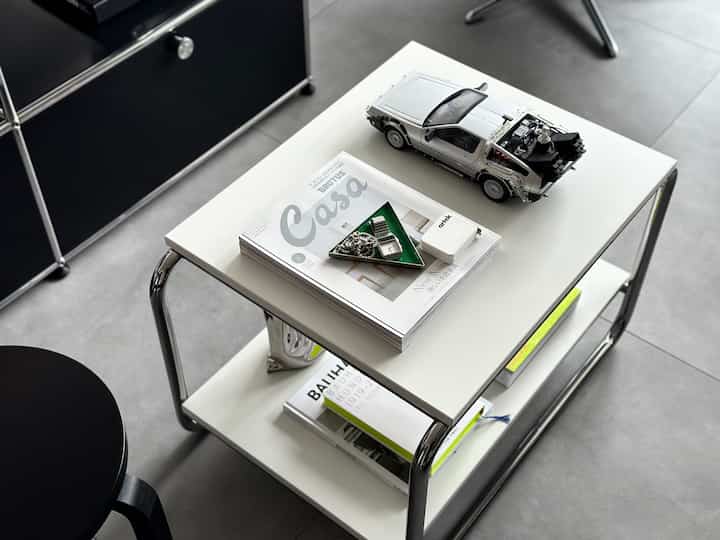 白とグレーのトーンの玄関スペース、シンプルなサイドテーブルと黒のスツールが配置されたミニマルなインテリア