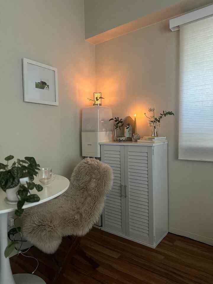 Beige-toned living room corner with white louvered cabinet, lit candles, dining table, and cozy fur throw chair