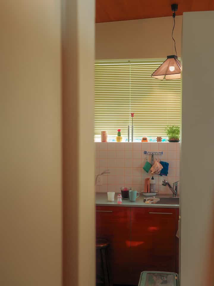 白いタイルと赤い下部キャビネット、窓のブラインドがある小さくてシンプルなキッチンの内装