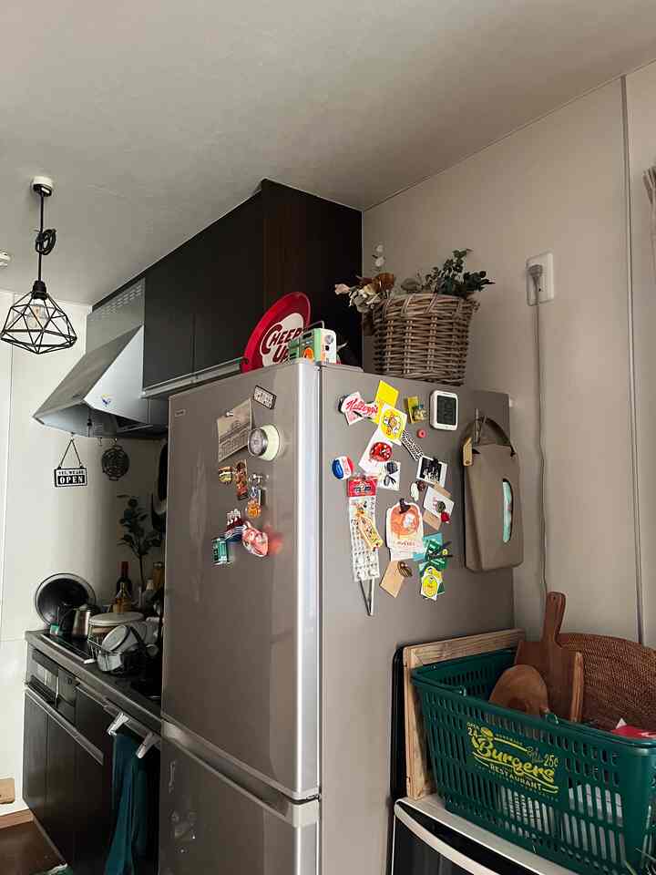 Compact kitchen with dark brown cabinets and silver refrigerator, featuring storage basket on top of fridge and various kitchen accessories