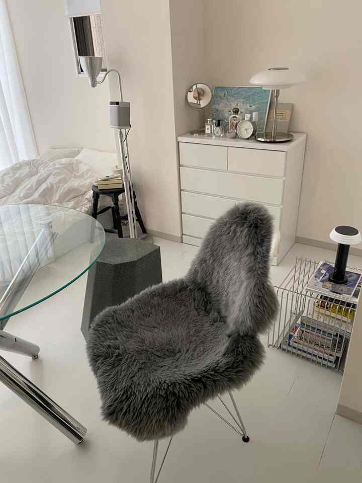 明るいホワイトとグレーのトーンの寝室空間、グレーのファースツールと白いチェスト、テーブルランプが配置されたモダンなインテリア