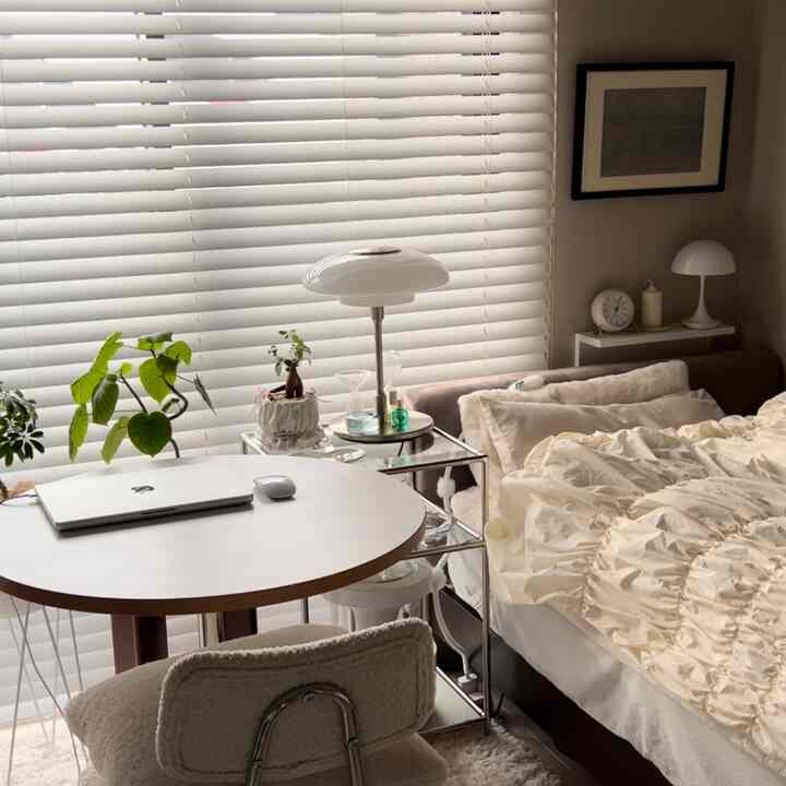 White and beige toned bedroom featuring bed and round table with laptop in a cozy and natural setting