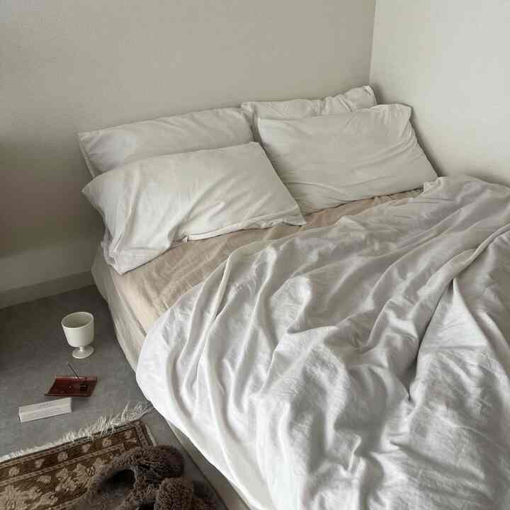 White and beige toned studio bedroom featuring a neatly made bed with white duvet covers creating a cozy atmosphere