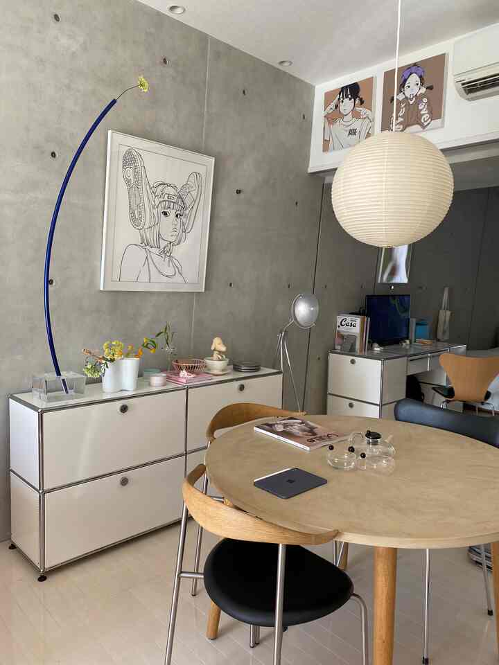 グレーのコンクリート壁と白いサイドボードが配置された、ナチュラルウッドの丸テーブルとペンダントライトのあるモダンなダイニング空間