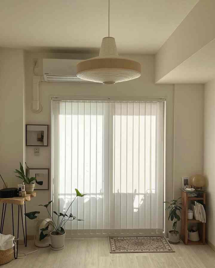 白とナチュラルカラーの1Kリビング、縦型ブラインドとペンダントライト、植物が配置された雰囲気のあるインテリア